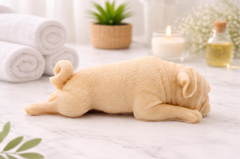 handmade vegan soap in the shape of a realistic sleeping pug dog lying flat, showing detailed wrinkles and fur texture, displayed in a spa-like setting with a candle and lavender.