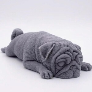 A detailed handmade vegan soap gift, sculpted in the shape of a pug dog lying flat on its stomach in a sleeping position, showing realistic skin folds and fur texture