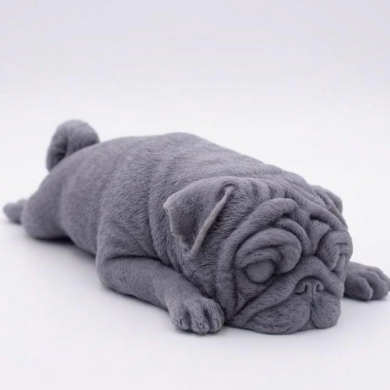 A detailed handmade vegan soap gift, sculpted in the shape of a pug dog lying flat on its stomach in a sleeping position, showing realistic skin folds and fur texture