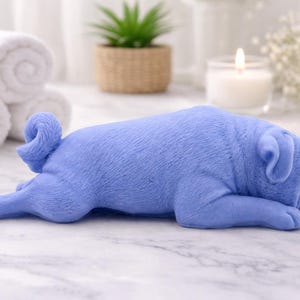 handmade vegan soap in the shape of a realistic sleeping pug dog lying flat, showing detailed wrinkles and fur texture, displayed in a spa-like setting with a candle and lavender.