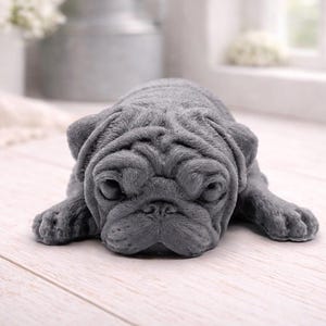 A detailed handmade vegan soap gift, sculpted in the shape of a pug dog lying flat on its stomach in a sleeping position, showing realistic skin folds and fur texture