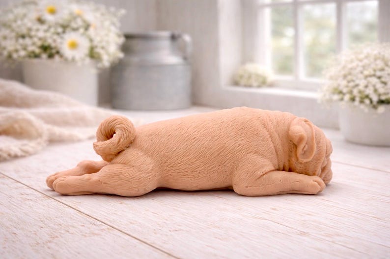 A detailed handmade vegan soap gift, sculpted in the shape of a pug dog lying flat on its stomach in a sleeping position, showing realistic skin folds and fur texture, displayed on a light wooden surface. Handmade in Blackpool