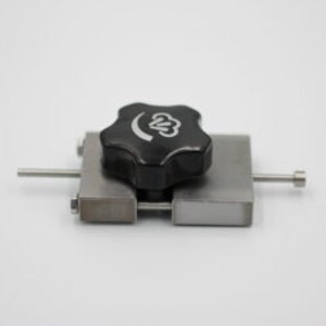 May include: A metal clamp with a black, star-shaped knob. The knob has a white graphic. The clamp has two metal bars with a metal rod extending from each side. The clamp is on a white background.