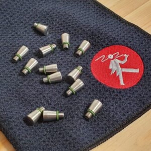 Op de afbeelding: Een close-up van een blauwe microvezeldoek met een rood logo met een stickfiguurtekening van een persoon die een penseel vasthoudt. De doek is bedekt met 13 zilveren metalen doppen met groene rubberen O-ringen.