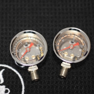 K&ouml;nnte beinhalten: Zwei verchromte Manometer mit roten Zeigern und einem Kaffeetassen-Symbol. Die Manometer sind mit "bar" beschriftet und haben Markierungen von 0,5 bis 2,5 bar und 4 bis 16 bar.