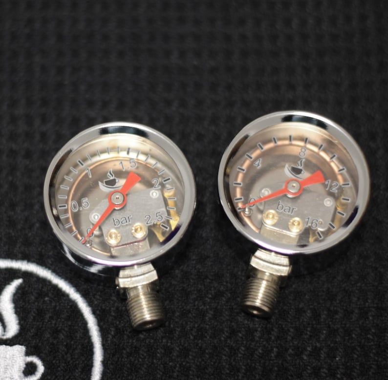 K&ouml;nnte beinhalten: Zwei verchromte Manometer mit roten Zeigern und einem Kaffeetassen-Symbol. Die Manometer sind mit "bar" beschriftet und haben Markierungen von 0,5 bis 2,5 bar und 4 bis 16 bar.