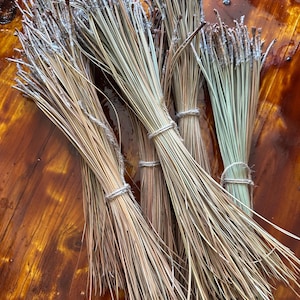 Puede incluir: Un manojo de agujas de pino secas, de color marrón claro y verde, atadas con un cordel. Las agujas son largas y delgadas, y están dispuestas en forma de abanico. El manojo está sobre una superficie de madera.