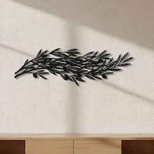 May include: A black metal wall art piece featuring a horizontal arrangement of olive branches with elongated leaves and small round olives. The design is symmetrical and elongated, showcasing a detailed silhouette of foliage and fruit in a flat finish.