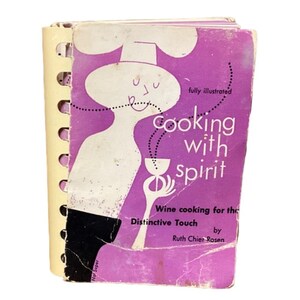 May include: Vintage cookbook titled "Cooking with Spirit" with a purple cover and spiral binding. The cover features a stylized illustration of a chef and text that reads "Wine cooking for the Distinctive Touch by Ruth Chier Rosen."