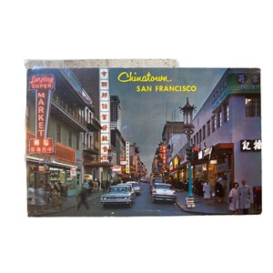 May include: Vintage postcard featuring a street scene in Chinatown, San Francisco. The image shows classic cars, neon signs, and buildings with Chinese characters. The words "Chinatown San Francisco" are displayed.