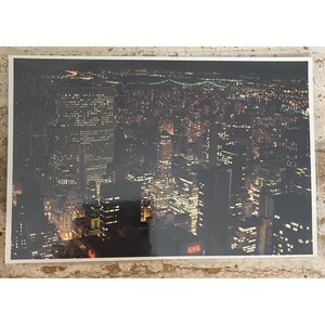 May include: A nighttime aerial photograph of a city skyline, illuminated by countless lights. The image captures the urban landscape with a bridge in the distance. The number "666" is visible on a building.