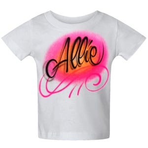 May include: White t-shirt with a pink and orange airbrushed design. The design features the name "Allie" in black script with a pink swirl accent. The shirt is a short-sleeved crew neck.