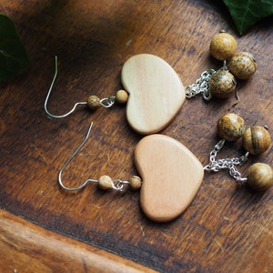 Puede incluir: Un par de pendientes de madera en forma de corazón con cuentas marrones y blancas moteadas que cuelgan de cada pendiente.