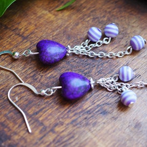 Könnte beinhalten: Lilafarbene herzförmige Ohrringe mit einer silbernen Kette und lila-weißen Perlen.