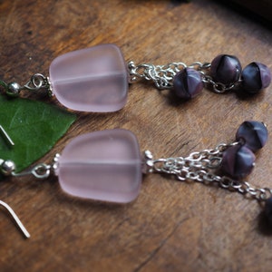 May include: A pair of earrings with pink glass teardrop-shaped pendants and silver chains with purple glass beads.