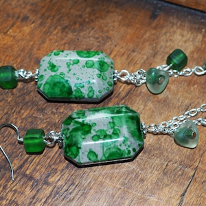 Peut inclure: Une paire de longues boucles d'oreilles en chaîne argentée avec des perles rectangulaires en résine verte et blanche et des perles en verre vert.