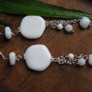 May include: White dangle earrings with a large white oval-shaped pendant and a chain with smaller white beads.