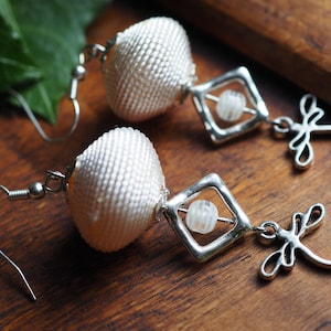Drop earrings in ecru silk thread and small assorted glass beads, finished with a dragonfly charm