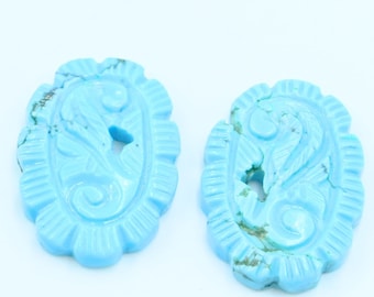 May include: Two light blue oval-shaped turquoise beads with a carved floral design. The beads have a scalloped edge.