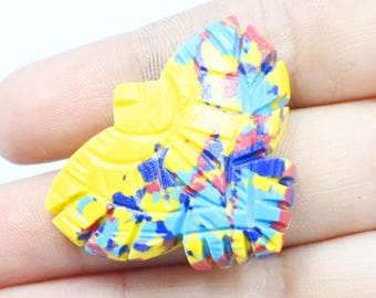 May include: A yellow, leaf-shaped decorative item with a colorful, abstract design. The item features a base color of yellow, with splashes of blue, red, and white. The item is held in a hand.