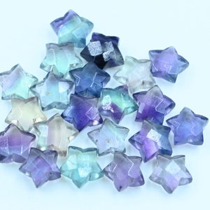 Può includere: Una collezione di perline di fluorite a forma di stella in tonalità di blu, viola e verde. Le perline sono sfaccettate e hanno una finitura scintillante e iridescente.