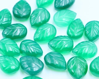 Puede incluir: Una colección de cabujones de piedra preciosa verde en forma de hoja. Los cabujones son lisos y pulidos, con una apariencia ligeramente translúcida.