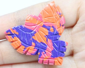 May include: A colorful leaf-shaped carving with orange, purple, and pink hues. The intricate details of the leaf's veins and edges are visible. The carving is held in a hand, showcasing its size and texture.
