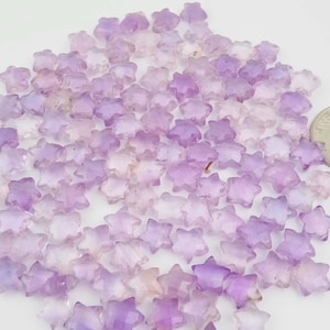May include: A large pile of purple star-shaped amethyst gemstone beads. The beads are faceted and have a light purple to dark purple colour gradient.