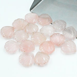 May include: A collection of pink rose quartz shell-shaped beads. The beads are smooth and polished, with a delicate, carved design.