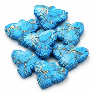 May include: A collection of eight turquoise-colored gemstone butterfly pendants. Each pendant has a detailed carved design with gold-colored veining. The pendants are arranged on a white background.