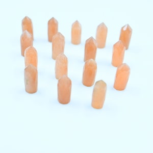 Puede incluir: Una colección de 14 pequeñas puntas de cristal de color naranja claro dispuestas en forma de corazón sobre un fondo blanco.