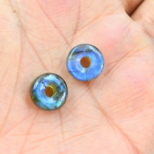 May include: Two iridescent blue and green donut-shaped labradorite gemstone beads with a hole in the center.