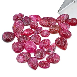 May include: A collection of 20 carved ruby gemstones in various shapes and sizes. The gemstones are a deep red color and have intricate floral designs.