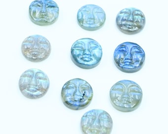 Könnte beinhalten: Zehn runde, blau-graue Labradorit-Cabochons mit geschnitzten Gesichtern. Jeder Cabochon hat ein einzigartiges, geschnitztes Gesicht mit geschlossenen Augen und einem ruhigen Ausdruck.