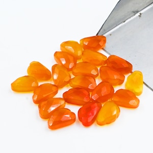 May include: A collection of orange and yellow faceted gemstone beads. The beads are heart-shaped and have a smooth, polished finish.