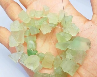 May include: A strand of light green, rough-cut gemstone beads. The beads are irregular in shape and size, with some being square and others being more triangular. The beads are strung on a thin wire.
