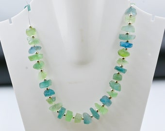 May include: A necklace made of light green, blue, and turquoise gemstone beads with silver spacers. The beads are irregular in shape and have a natural, rough texture.