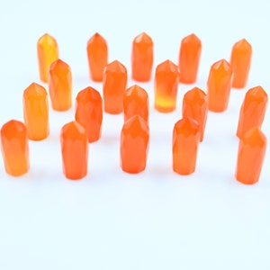 Pode incluir: Uma coleção de vinte pontas de cristal de cornalina laranja dispostas simetricamente sobre um fundo branco.