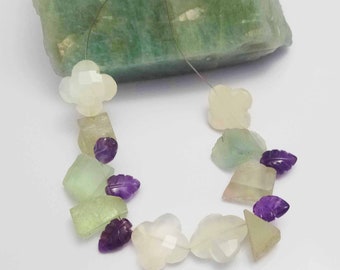 May include: A strand of gemstone beads featuring a mix of light green, white, and purple beads. The beads are carved into different shapes, including leaves, flowers, and squares.