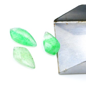 May include: Three green gemstone cabochons in a marquise shape, spilling out of a metal tray.