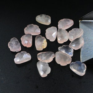 May include: A collection of 15 pink rose quartz cabochons, each with a unique, faceted, cloud-shaped design. The stones are translucent and have a slight shimmer.