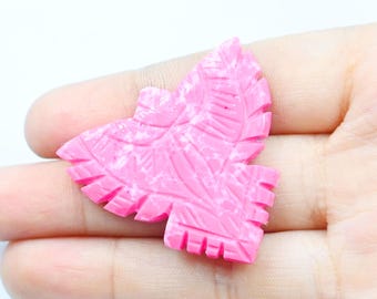 May include: A pink butterfly-shaped carving with white marbling. The butterfly has detailed wing patterns and a textured surface. The carving is held in a hand against a white background.
