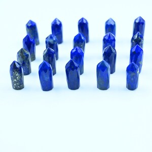 Pode incluir: Uma coleção de 18 pontas de cristal de lapis-lazúli azul dispostas em filas sobre um fundo branco.