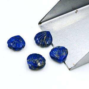 May include: Four blue lapis lazuli gemstone cabochons carved in the shape of a seashell. The gemstones have a dark blue color with gold flecks throughout.