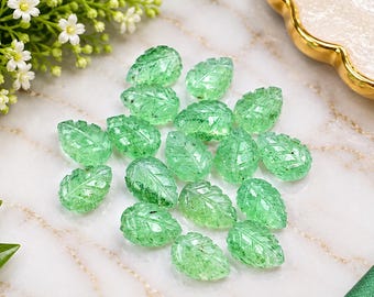 May include: A collection of fifteen translucent green gemstone beads carved into the shape of leaves. Each bead features detailed vein patterns on the surface, with a polished finish that catches the light, showcasing internal inclusions and variations.