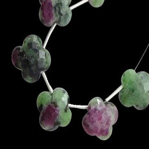 May include: A strand of green and pink clover-shaped gemstone beads. The beads are strung on a silver wire.