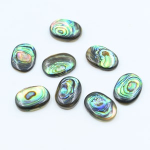 May include: Eight oval-shaped abalone shell cabochons with iridescent green, blue, and brown colors. The cabochons are smooth and polished.
