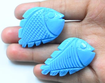 May include: Two blue carved fish pendants. The fish are detailed with scales and fins.