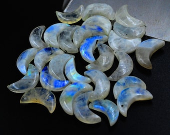 May include: A collection of crescent moon shaped rainbow moonstone beads. The beads are a milky white color with iridescent blue and green hues.