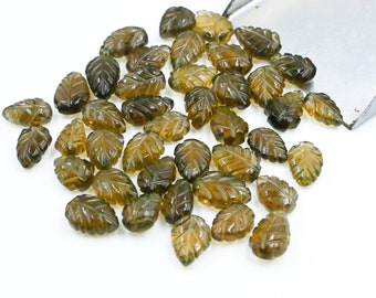 May include: A collection of green and brown leaf-shaped gemstone beads. The beads are carved with intricate details and have a translucent appearance.